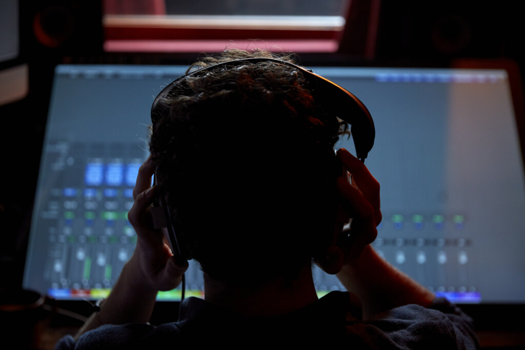 Man working in music studio wearing headphones using large computer screen shot from behind